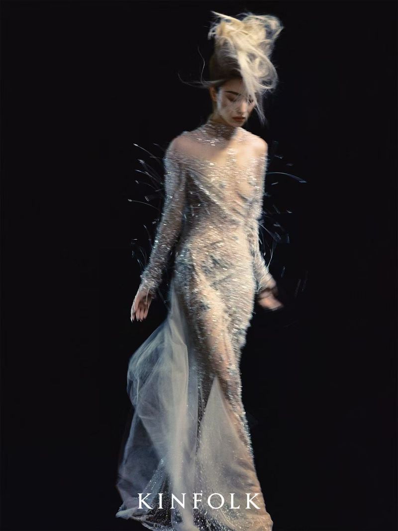 Woman in shimmering gown with high hair against dark background. Editorial fashion shot with dramatic lighting and elegant, ethereal style.