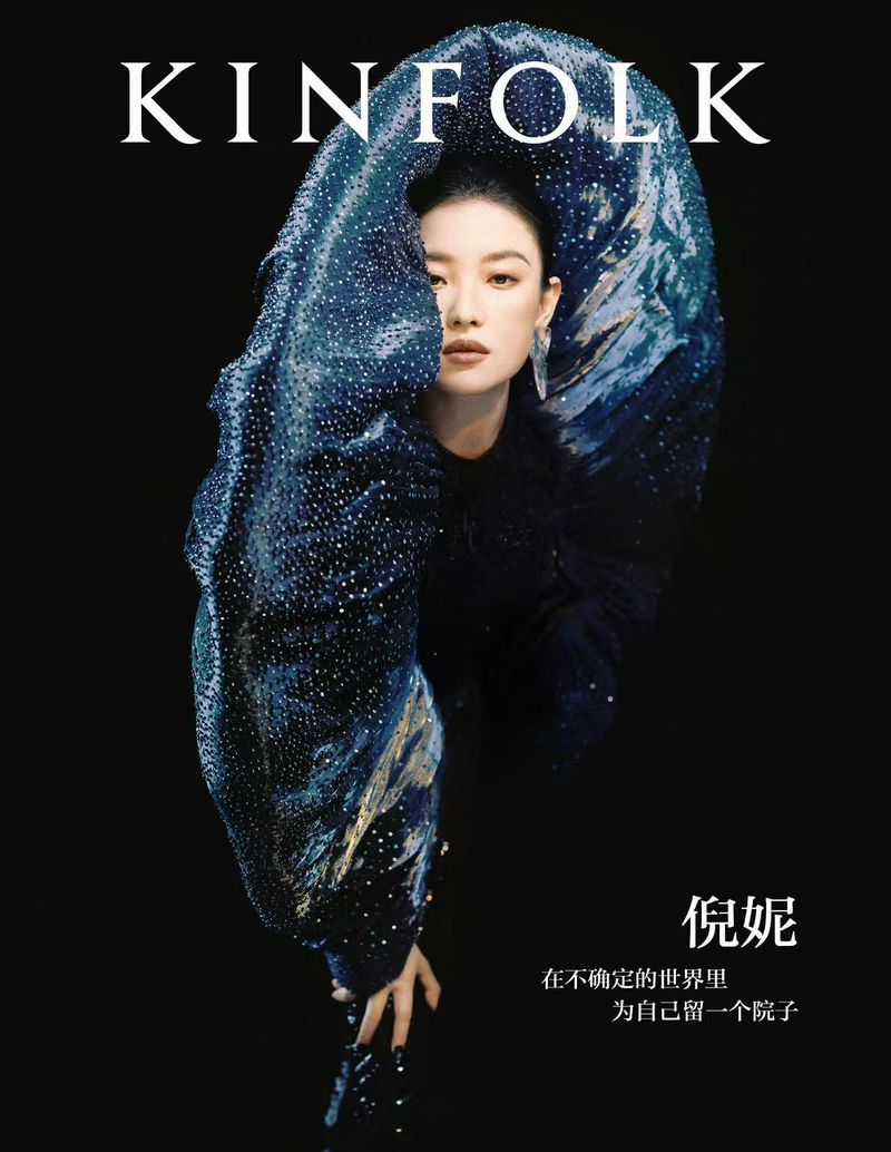 Magazine cover featuring a woman with a striking blue, patterned headpiece against a dark backdrop, showcasing beauty and style.