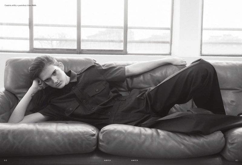 Model Tia Edney lying on a leather sofa wearing a dark utility shirt and trousers for Amica magazine editorial TOMBOYish.