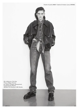 Model wearing a dark leather bomber jacket, denim shirt, and jeans against a plain white studio backdrop.