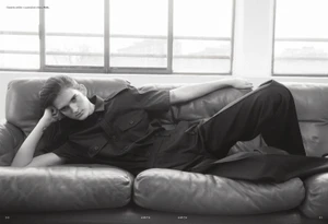 Model Tia Edney lying on a leather sofa wearing a dark utility shirt and trousers for Amica magazine editorial TOMBOYish.