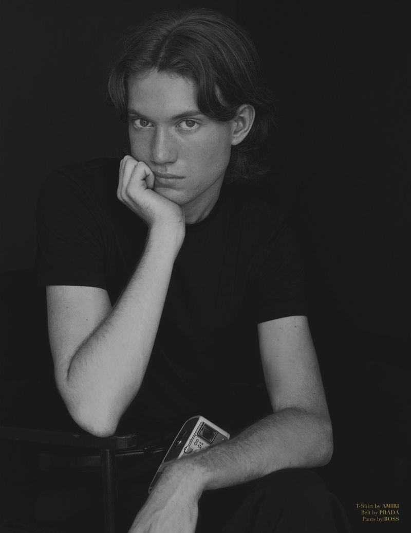 Portrait of a young man resting his chin on his hand in front of a dark background wearing a black t-shirt