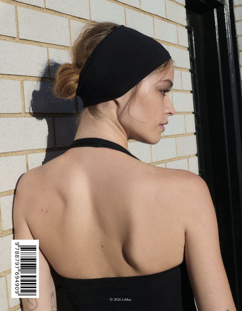 Woman in black halter top and headband faces right, showcasing her bare back and hair styled in a bun in an outdoor setting.