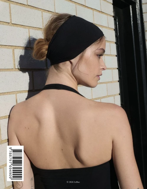 Woman in black halter top and headband faces right, showcasing her bare back and hair styled in a bun in an outdoor setting.
