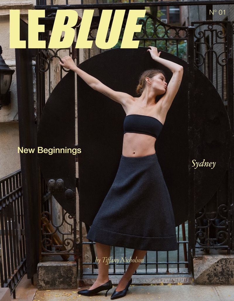 Magazine cover featuring a woman in a black tube top and skirt, standing in front of a black gate with the title 'LE BLUE'.