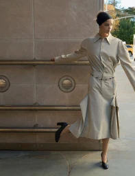 Model wearing a tan skirt and shirt set with a black headband standing against a concrete building exterior