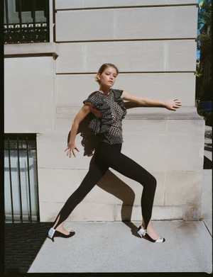 Model in black ruffled top and stirrup leggings posing against an architectural stone building exterior