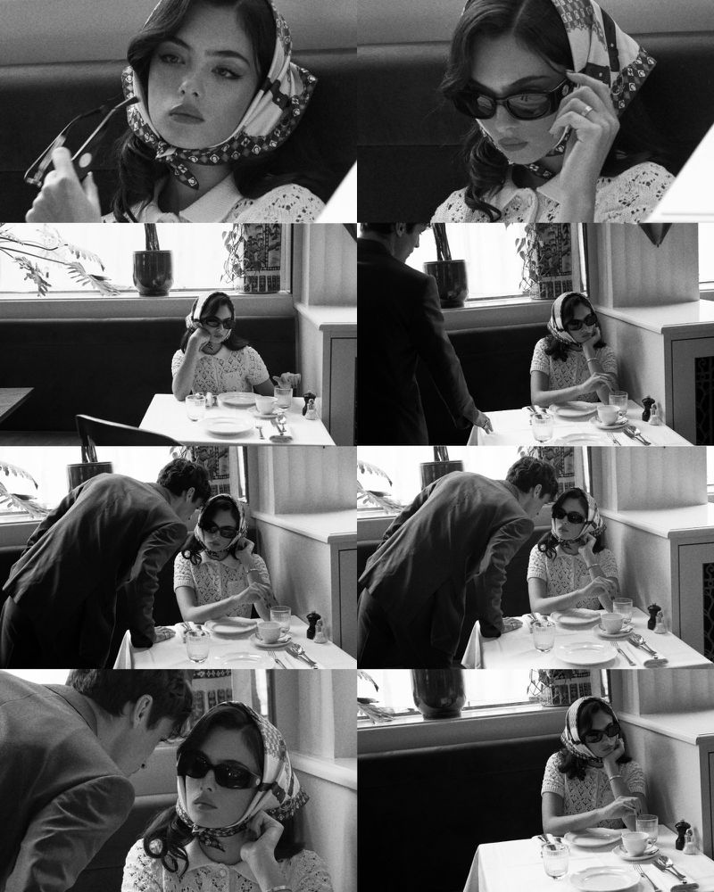 Monochrome shot in a retro restaurant setting shows a woman in a scarf and sunglasses, being approached by a man in a suit.