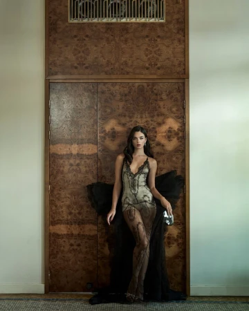 Model Deva Cassel in a lace slip dress and dark wrap standing against an ornate wooden door for Vanity Fair France editorial