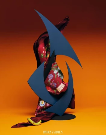 Still life featuring a silk scarf with floral design and a blue geometric sculpture against a gradient orange background.