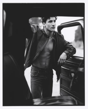 Model leaning against an open car door wearing a dark jacket for Numero Homme editorial