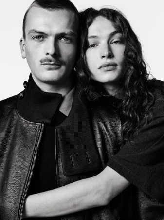 Black-and-white portrait of a couple in a close embrace. The man has a mustache, and the woman has long, curly hair and a serious facial expression.