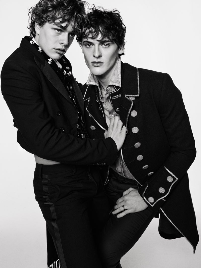 Black and white portrait of two adult men in fashionable black jackets posing in front of a white studio background, studio lighting.
