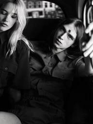 Black and white portrait of a blond woman and a dark-haired man seated inside a vehicle for Numero Homme editorial