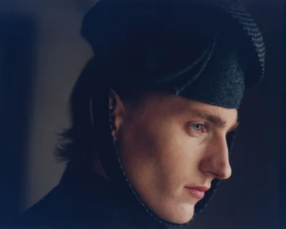 Profile portrait of a male model wearing a dark structured hat and dark top for SHADOWPLAY Magazine