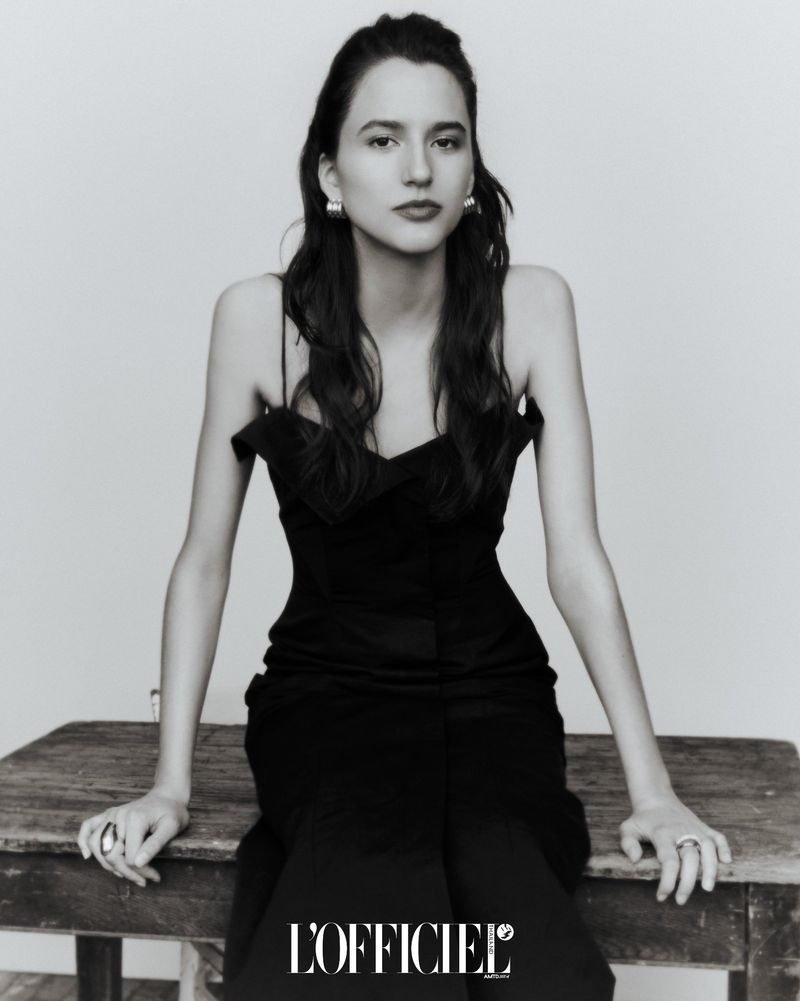 Model Belu Porto in a black dress seated on a wooden table for L'Officiel Thailand project Multiple Identities