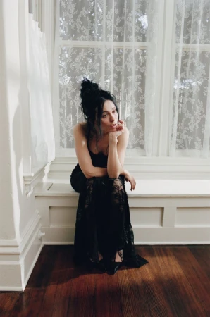 Model Marta Pozzan seated on a window bench wearing a dark lace dress for Puss Puss Magazine photographed by Chloé Horseman.