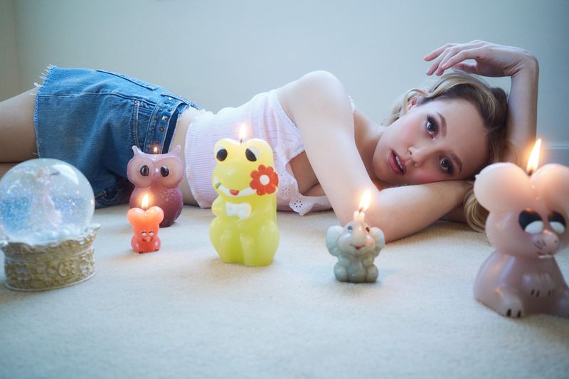 Young woman lying on the floor surrounded by animal-shaped candles and a snow globe in a soft, ambient light.