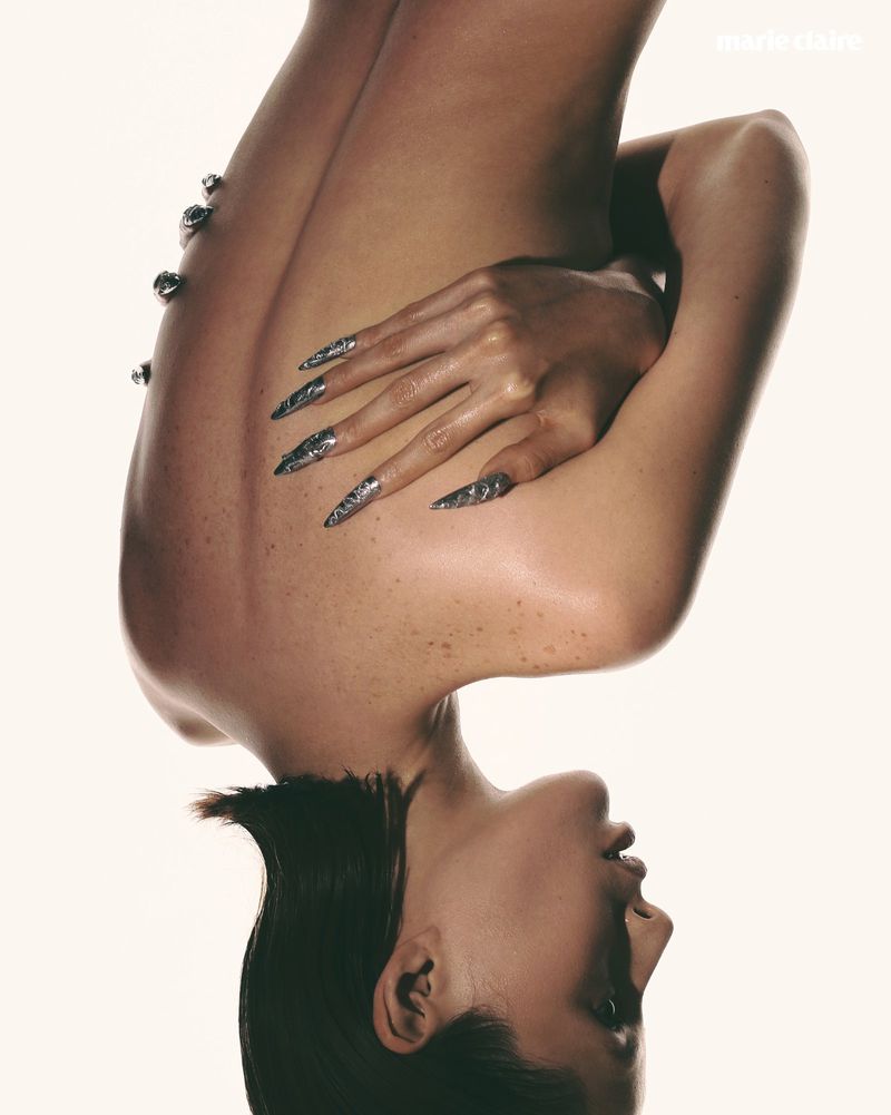 Artistic portrait of a woman inverted against a bright backdrop, showcasing her face, shoulder, upper back, and long, silver nails.