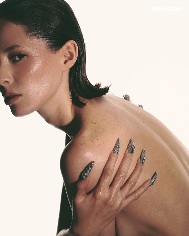 Striking beauty portrait of a woman with artistic silver fingernails, against a clean white background, showcasing skin texture and minimalist aesthetic.