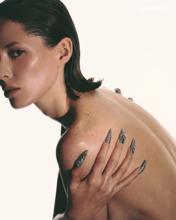 Striking beauty portrait of a woman with artistic silver fingernails, against a clean white background, showcasing skin texture and minimalist aesthetic.