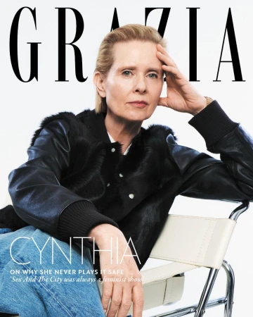Cynthia Nixon magazine cover. Portrait of an adult woman with blonde hair wearing a black jacket and blue jeans sitting on a chair.