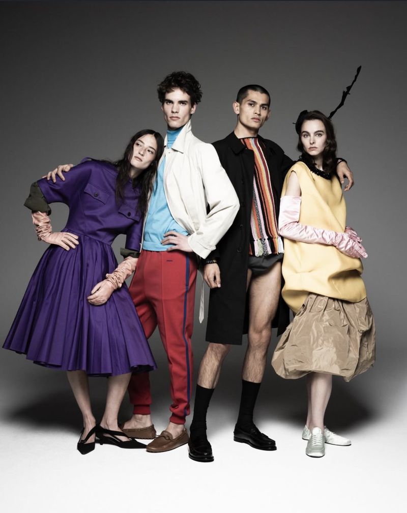 Fashion editorial image featuring four models in colourful clothing posing against a grey backdrop in a studio, capturing a modern style.