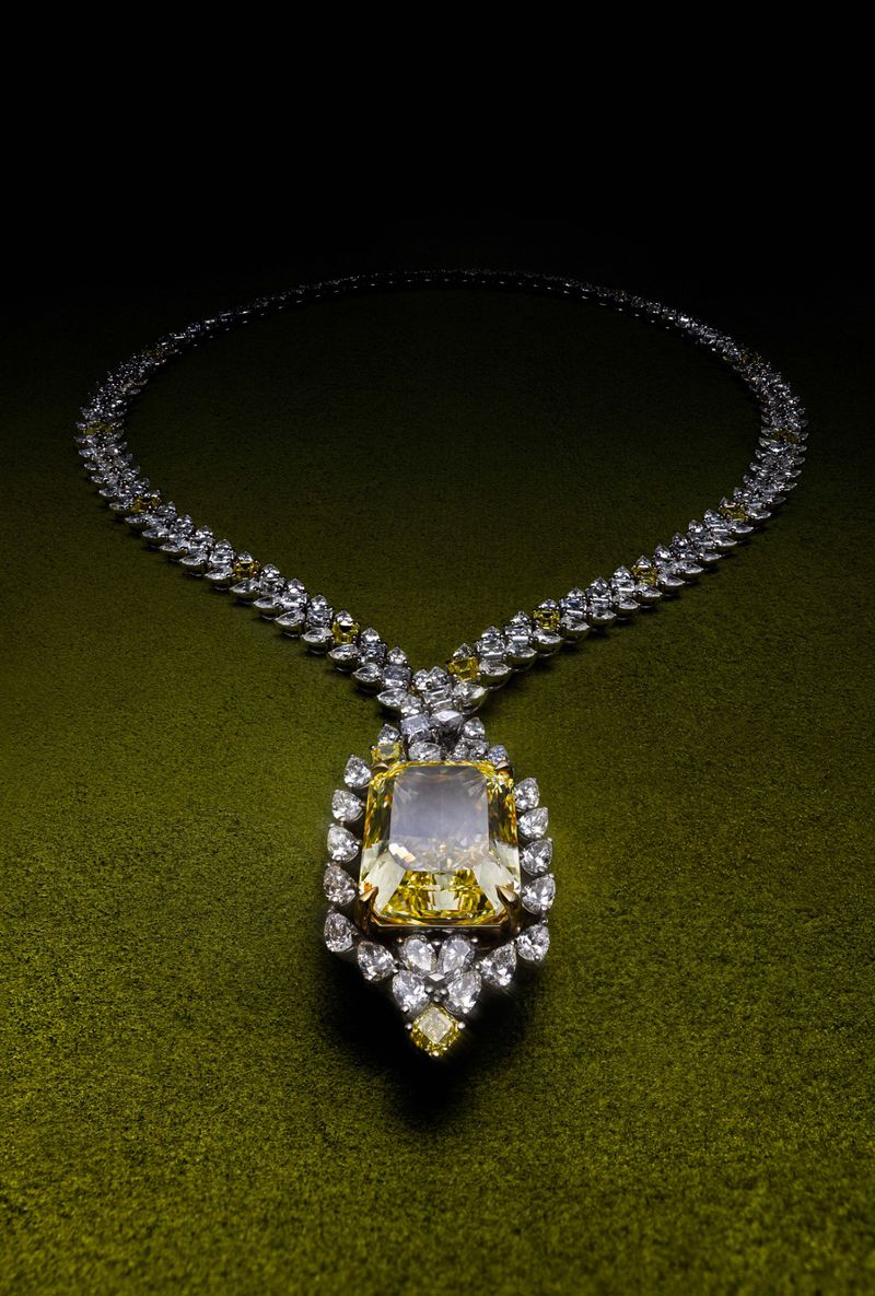 A diamond necklace featuring a large, yellow, square-cut diamond pendant surrounded by smaller white diamonds on a green background.