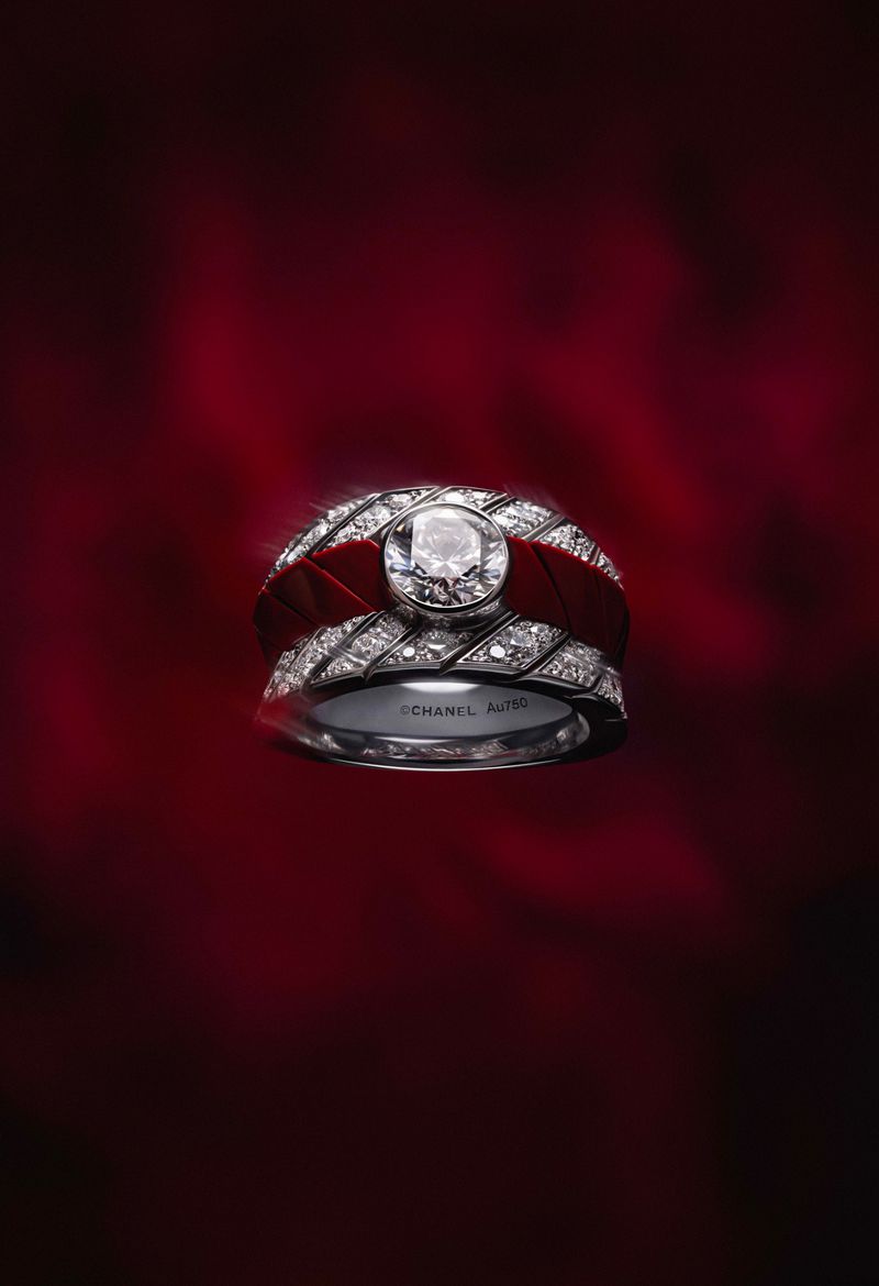 Close-up of two Chanel rings, one silver with diamonds and another with a red band and central diamond, against a dark red background.