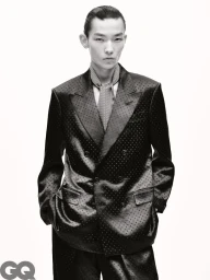 Model wearing a dark double-breasted polka dot suit jacket and patterned necktie against a white studio background.
