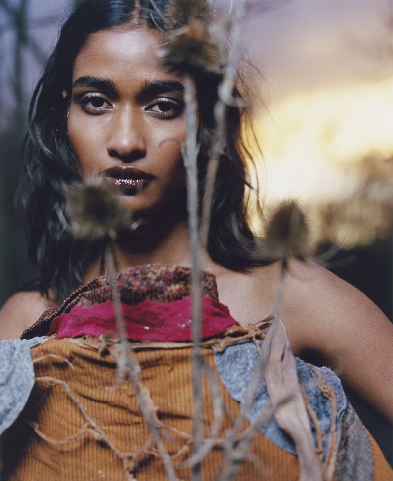Portrait of a woman with dark hair and brown skin, holding a textured fabric in an outdoor setting with a blurred background and warm light.