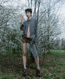 Model in plaid shirt and shorts standing among blooming trees in a forest for Atmos Magazine