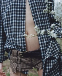 Close-up of a person wearing an open blue and white plaid shirt and brown patterned shorts outdoors
