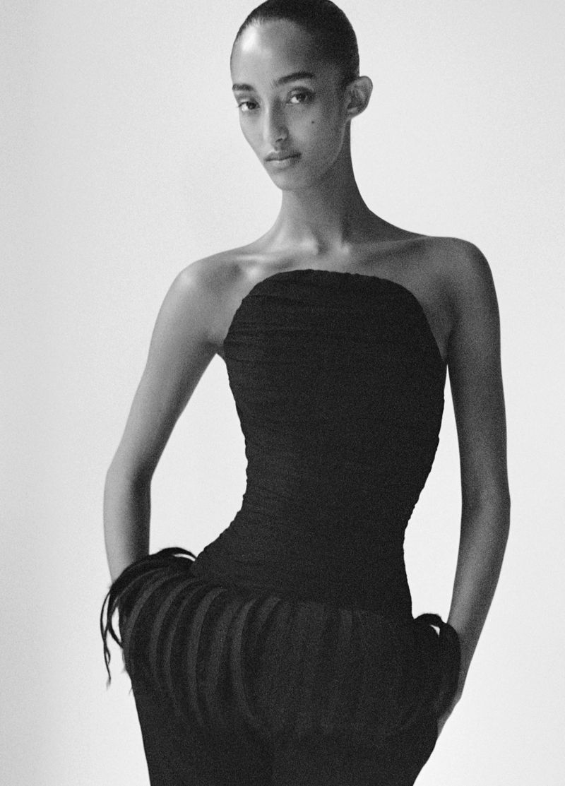 Elegant black and white studio portrait of a fashion model wearing a sleeveless black dress with a textured, decorative skirt.