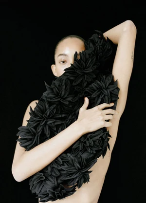 Mona Tougaard holding a cluster of black fabric flowers against a black background for Purple Magazine