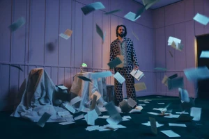 Shazad Latif standing in a purple room with loose pages falling around him for a Schön Magazine editorial portrait.