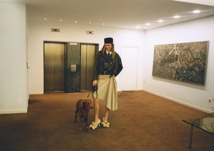 Model wearing a black jacket and cream skirt holding a dog on a leash inside a hotel lobby