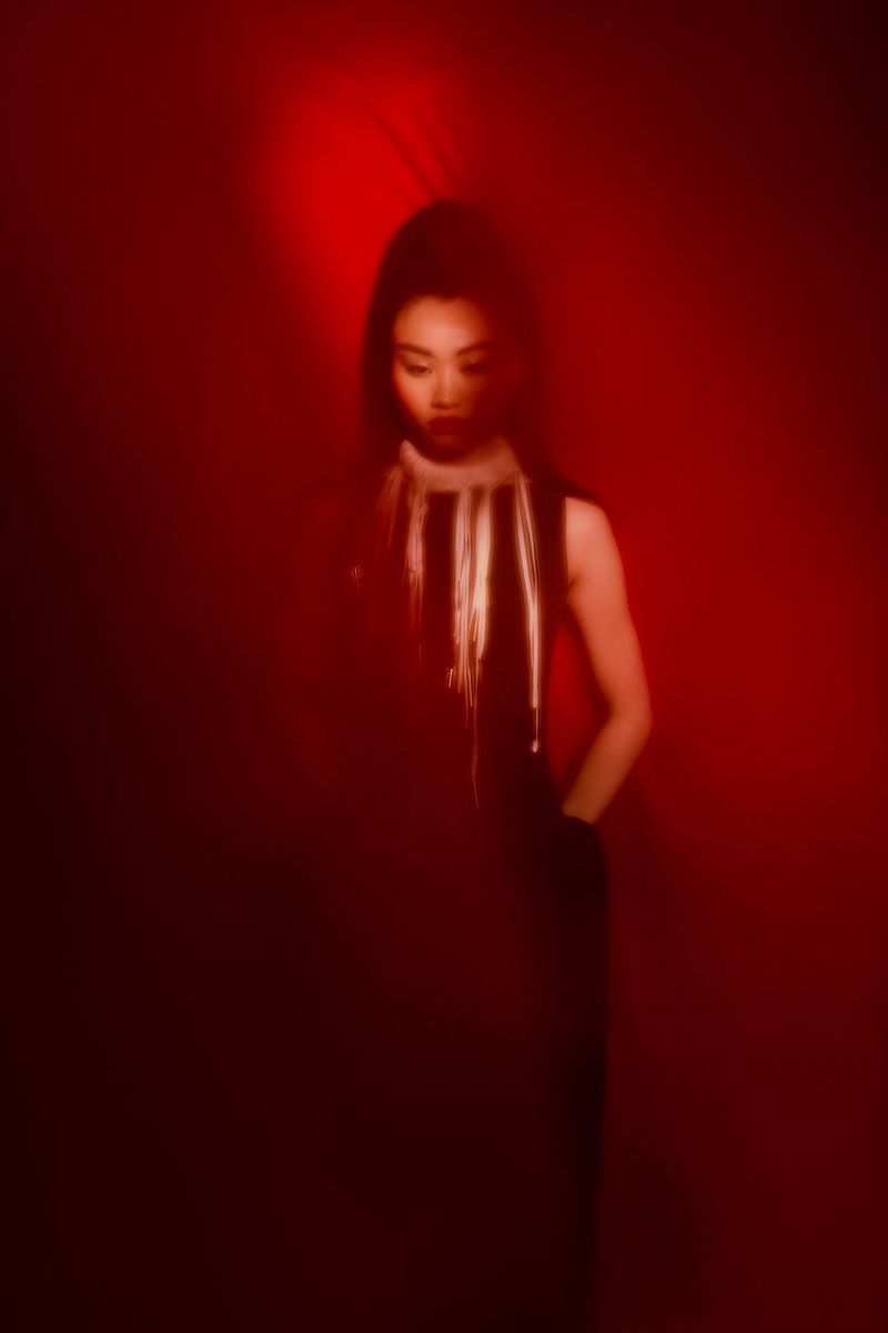Portrait of a woman in a black dress with white accents, set against a deep red background with soft, diffused lighting.