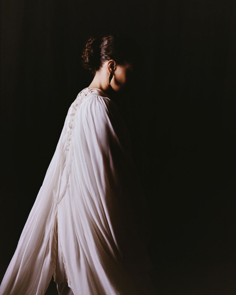 Elegant woman in a flowing white dress, side view, against a dark background, showcasing soft lighting and graceful movement.