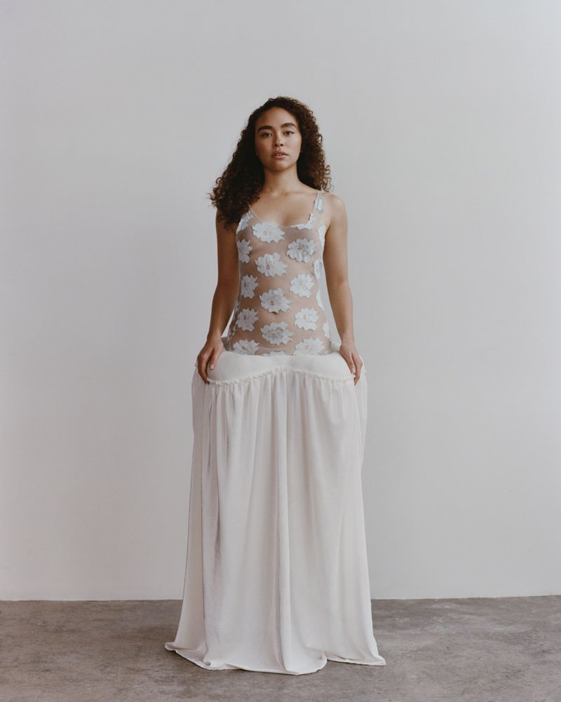 Adult female poses in a white floral lace top and a long white skirt in a studio with neutral background, fashion portrait, studio lighting.