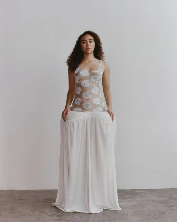 Adult female poses in a white floral lace top and a long white skirt in a studio with neutral background, fashion portrait, studio lighting.
