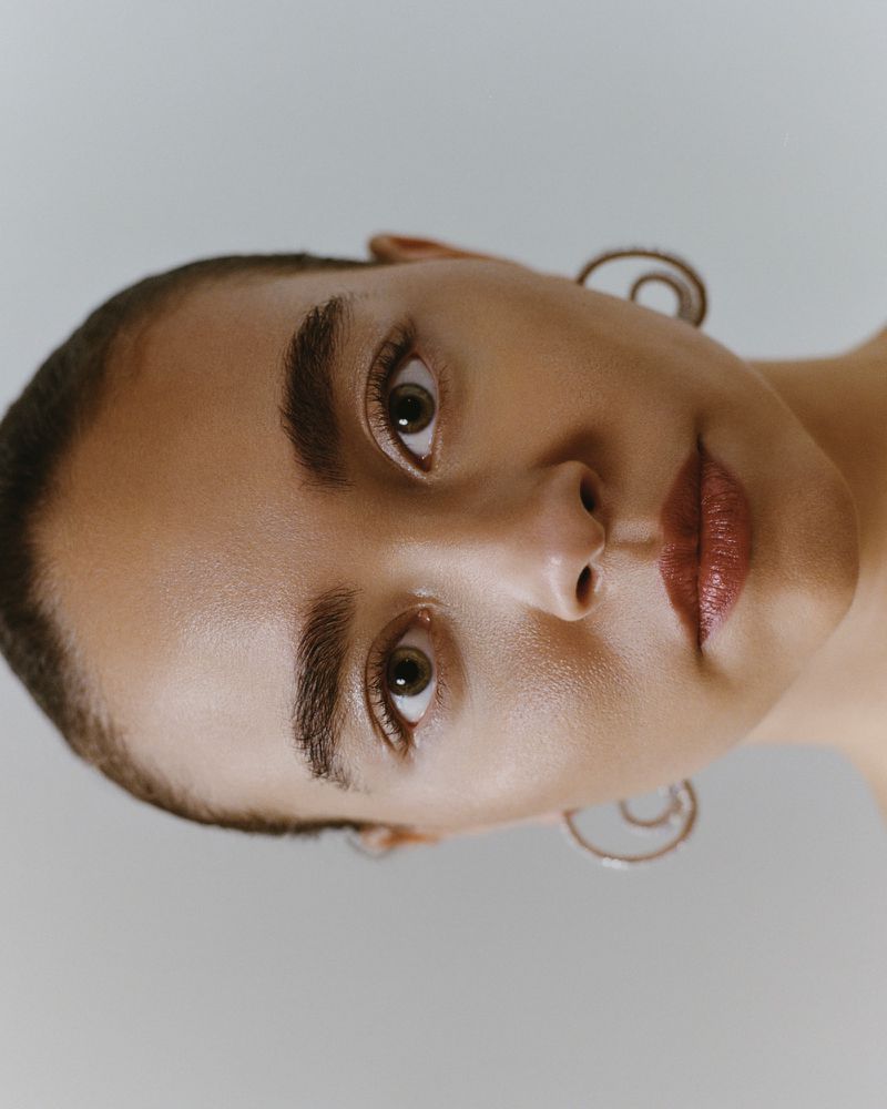 Close-up portrait of a woman with short hair and earrings against a neutral background, captured with soft lighting.