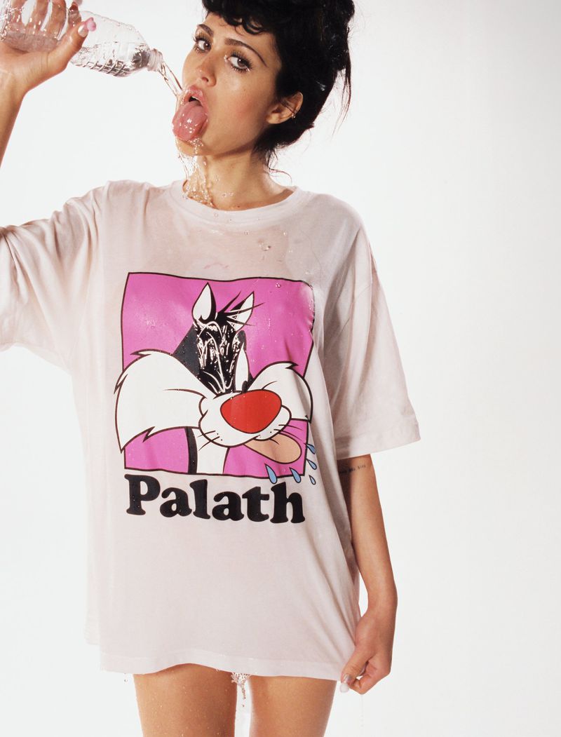 Woman in oversized t-shirt drinks from water bottle against a white backdrop. Focus on fashion and hydration.