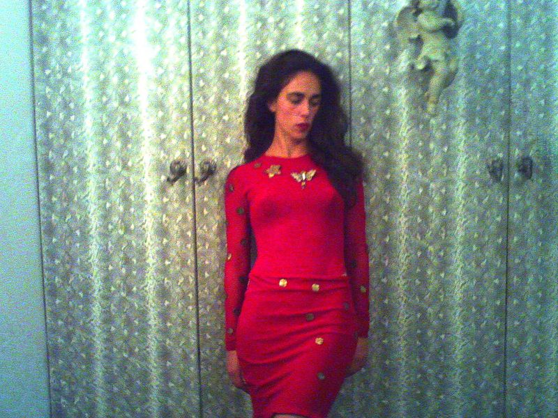 Adult female in a red dress poses in front of a closet with a white and gray patterned door and a decorative angel.