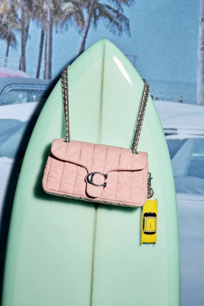 Pink quilted leather shoulder bag with chain strap displayed on a mint green surfboard against a beach backdrop
