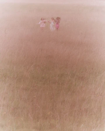 A group of young women are running hand-in-hand through a tall grass field on a hazy day, creating a dreamy, carefree atmosphere.