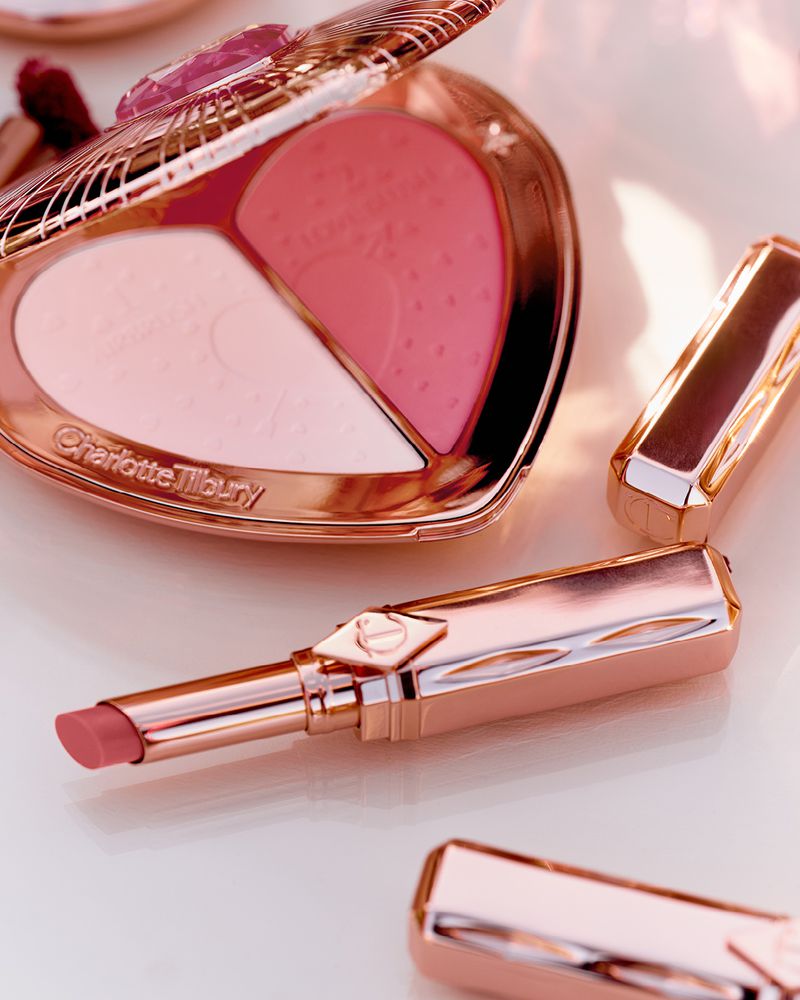 Close-up of rose gold Charlotte Tilbury makeup compact and lipsticks, featuring pink blush and powders in a heart-shaped case.