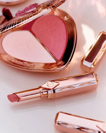 Close-up of rose gold Charlotte Tilbury makeup compact and lipsticks, featuring pink blush and powders in a heart-shaped case.