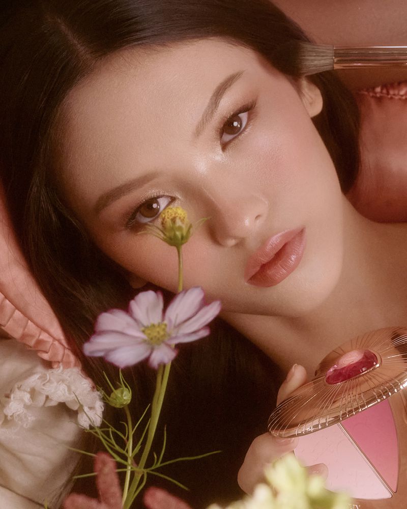 Close-up beauty shot of a woman applying makeup with a brush, fair skin, brown hair, eye-level angle in indoor setting.