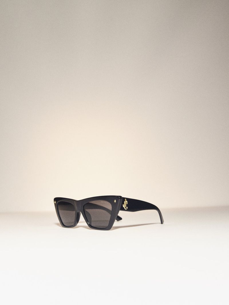 Black cat-eye sunglasses with the Jimmy Choo logo are prominently displayed against a white background, showcasing high-fashion eyewear.
